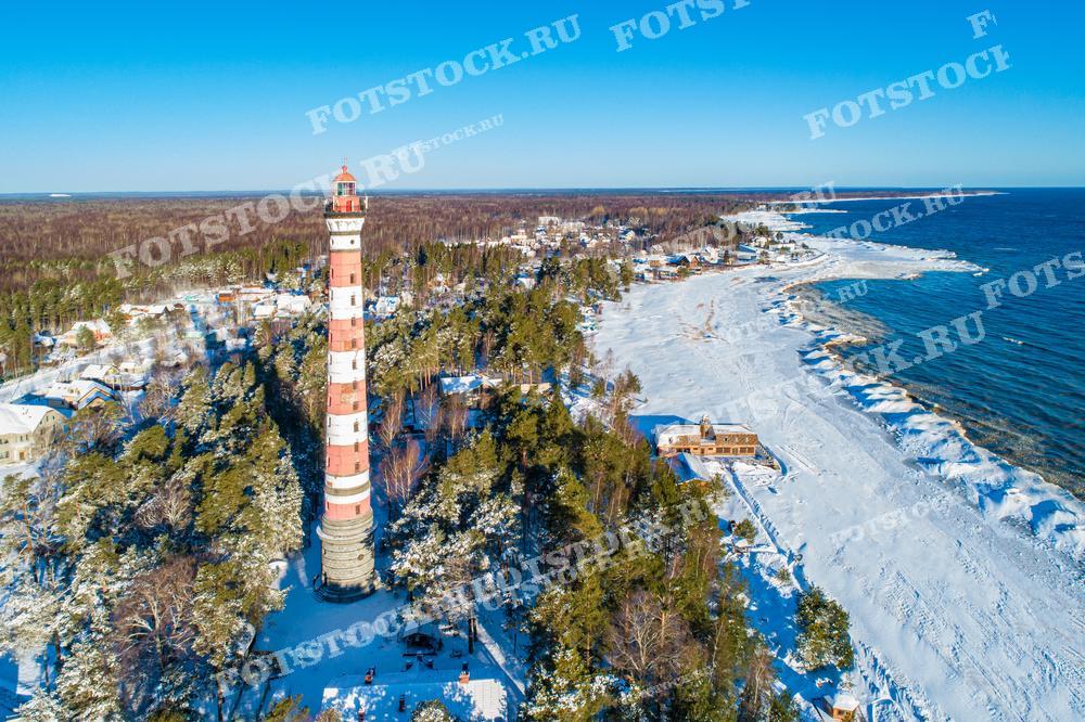 Эта фотография с высоты показывает Осиновецкий маяк, расположенный на берегу Ладожского озера, окружённый снежным лесом и ледяным покровом на воде. Маяк является важным навигационным объектом и историческим памятником региона. Этот снимок идеален для иллюстрации статей о маяках России, зимних пейзажах и исторической архитектуре.